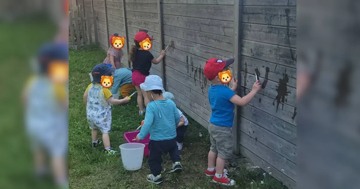 Enfants dessinant à l'eau sur la palissade en bois du jardin d'une micro-crèche à Sélestat